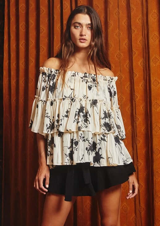 Bucket List Style# T1484 | Ladies Floral Print Tiered Off Shoulder Top with Merrow stitch detailing lurex chiffon in Cream with Black Floral Print | Made in USA