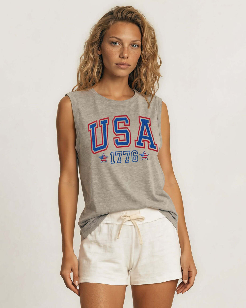 Glitter USA varsity graphic muscle tee with 1776 & flag star accents. Made in USA, relaxed fit, 75% cotton. Perfect for 4th of July. Sizes S-L.