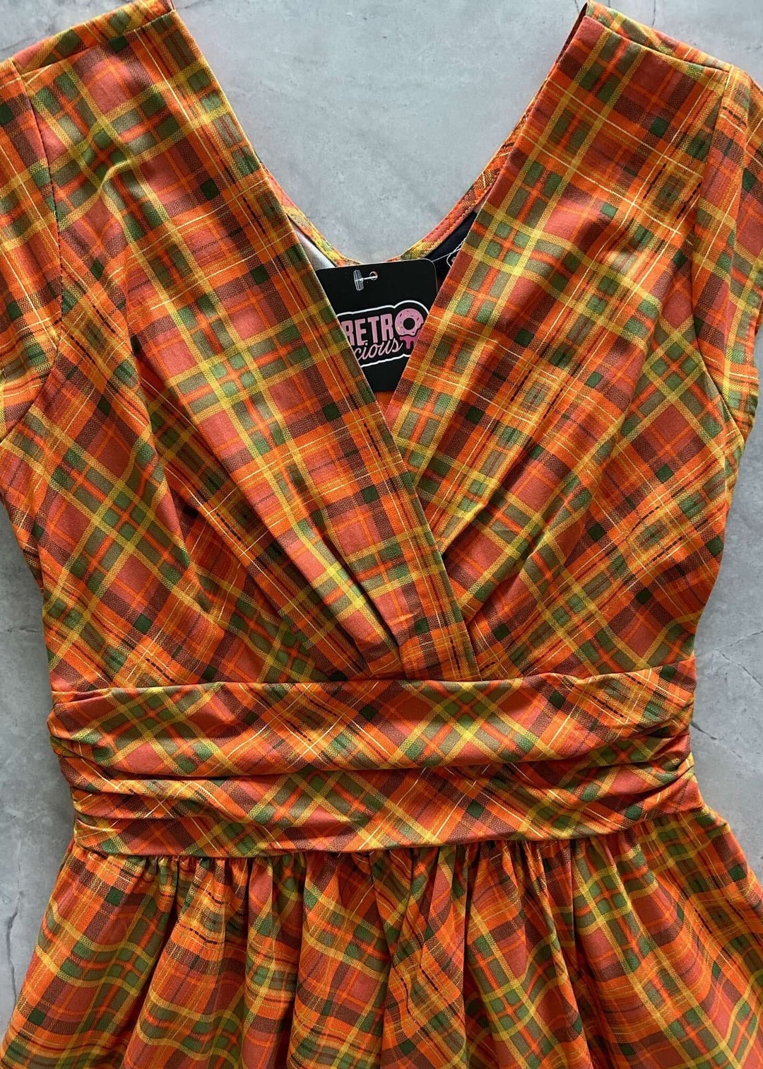 Made in USA The Greta is everything you could want and more! Shown in our Orange Plaid print, this vintage style cotton knee length dress features a gathered surplice neckline, cummerbund waist with figure flattering gathers, a vintage inspired twirl-worthy skirt with hidden side pockets, and a back zippered closure.