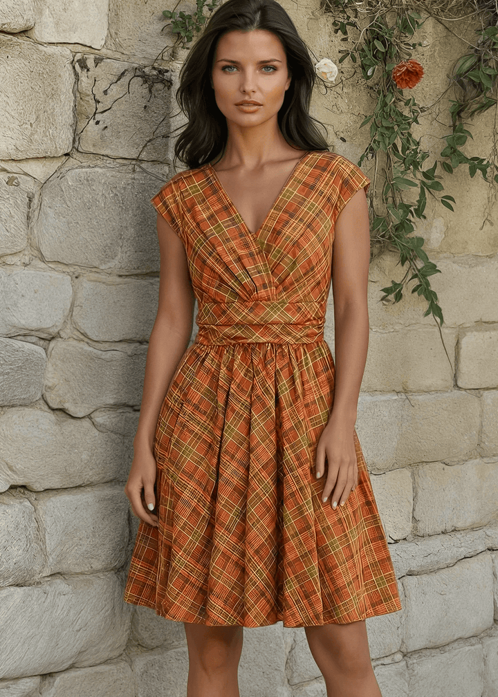 Made in USA The Greta is everything you could want and more! Shown in our Orange Plaid print, this vintage style cotton knee length dress features a gathered surplice neckline, cummerbund waist with figure flattering gathers, a vintage inspired twirl-worthy skirt with hidden side pockets, and a back zippered closure.