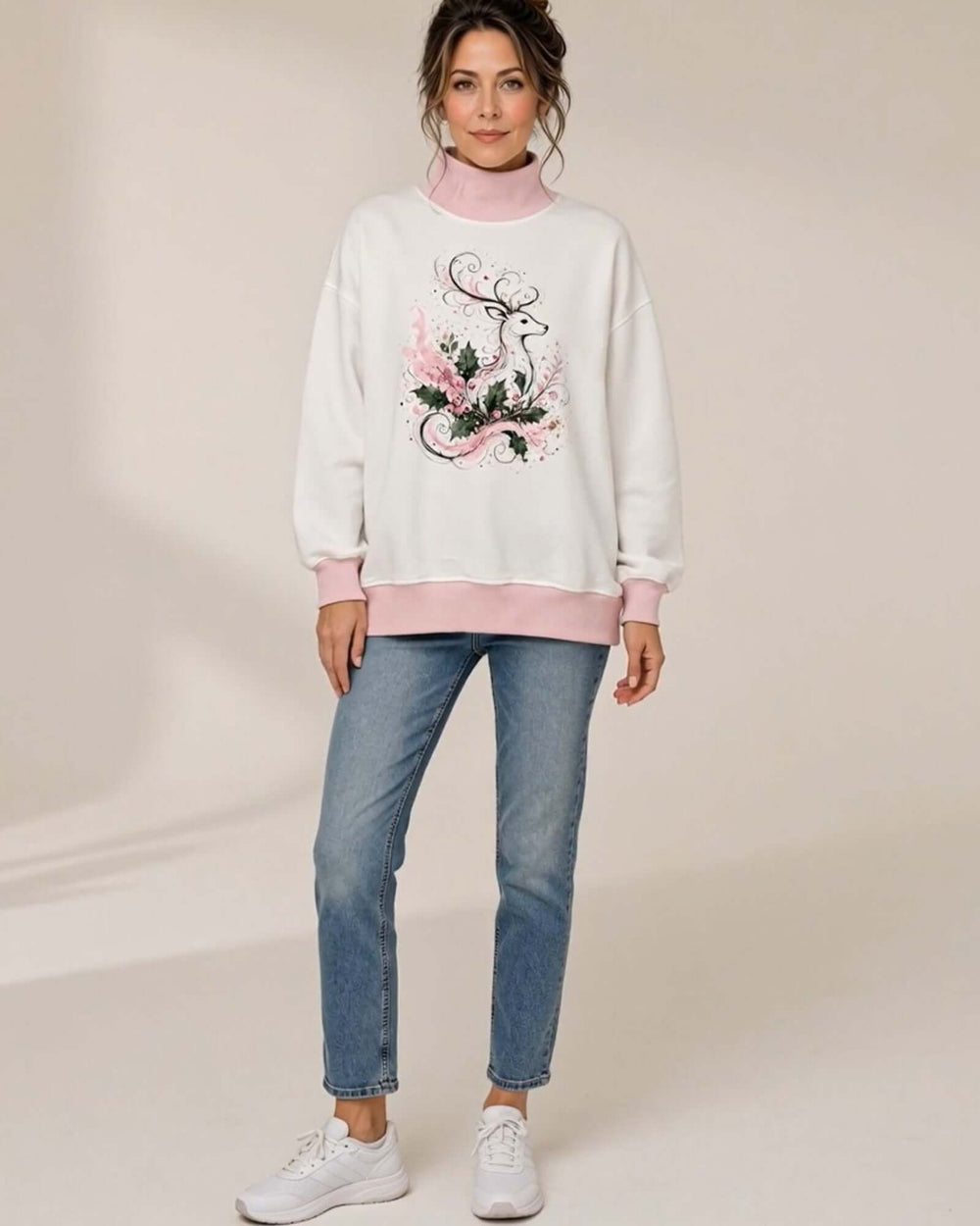 Women's white oversized mock neck sweatshirt with pink ribbed trim featuring the Whimsical Reindeer Holiday Graphic design, front full-length view styled with blue jeans and white sneakers, Made in USA