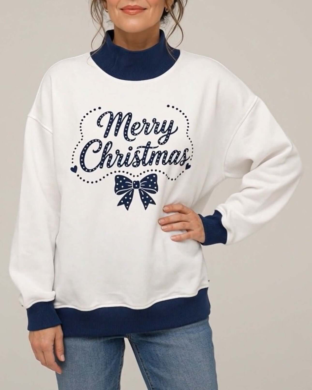 Women's white oversized mock neck sweatshirt with navy ribbed trim featuring the Navy Christmas Bow design, front view, hand on hip, Made in USA