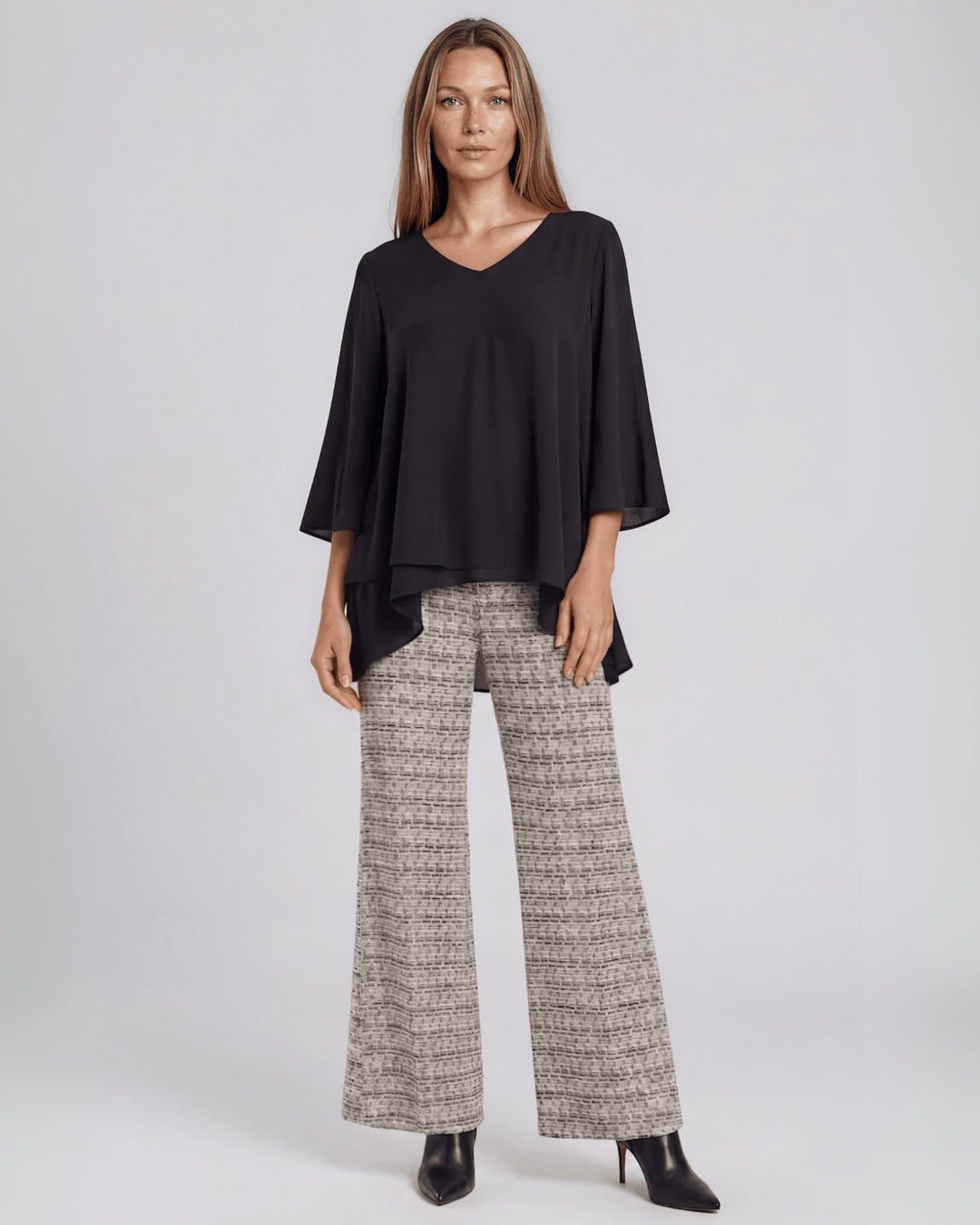 Black dressy V-neck tunic top with mid-length bell sleeves and an overlapping high-low hem that creates a flowy, layered silhouette in lightweight 100% polyester. Made in USA.