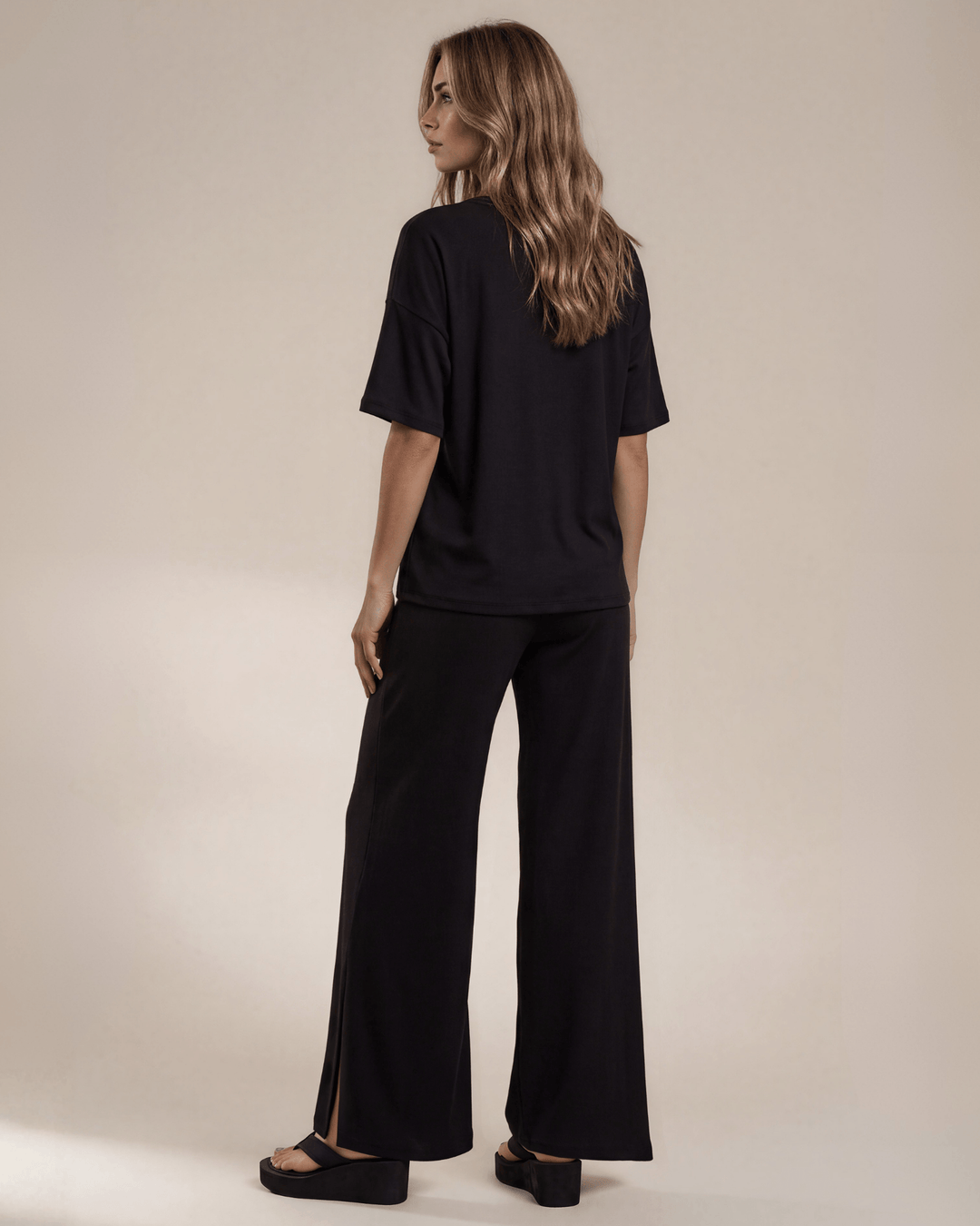 "Black two-piece loungewear set featuring a relaxed-fit short-sleeve crew neck tee with a chest pocket and wide-leg pants with split hems and an elastic waistband, in a soft stretch fabric blend. Made in USA."