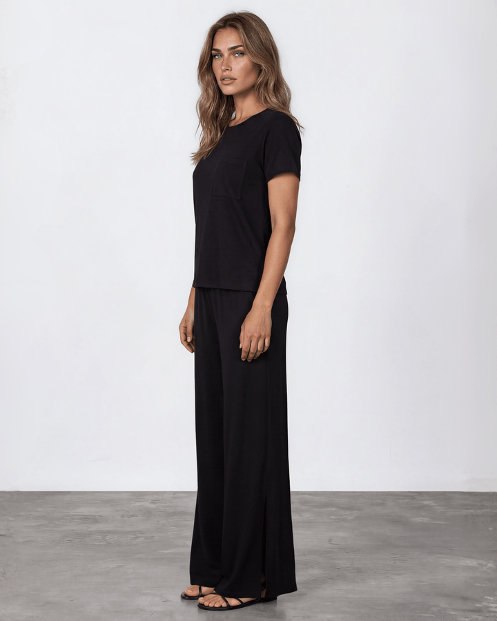 "Black two-piece loungewear set featuring a relaxed-fit short-sleeve crew neck tee with a chest pocket and wide-leg pants with split hems and an elastic waistband, in a soft stretch fabric blend. Made in USA."