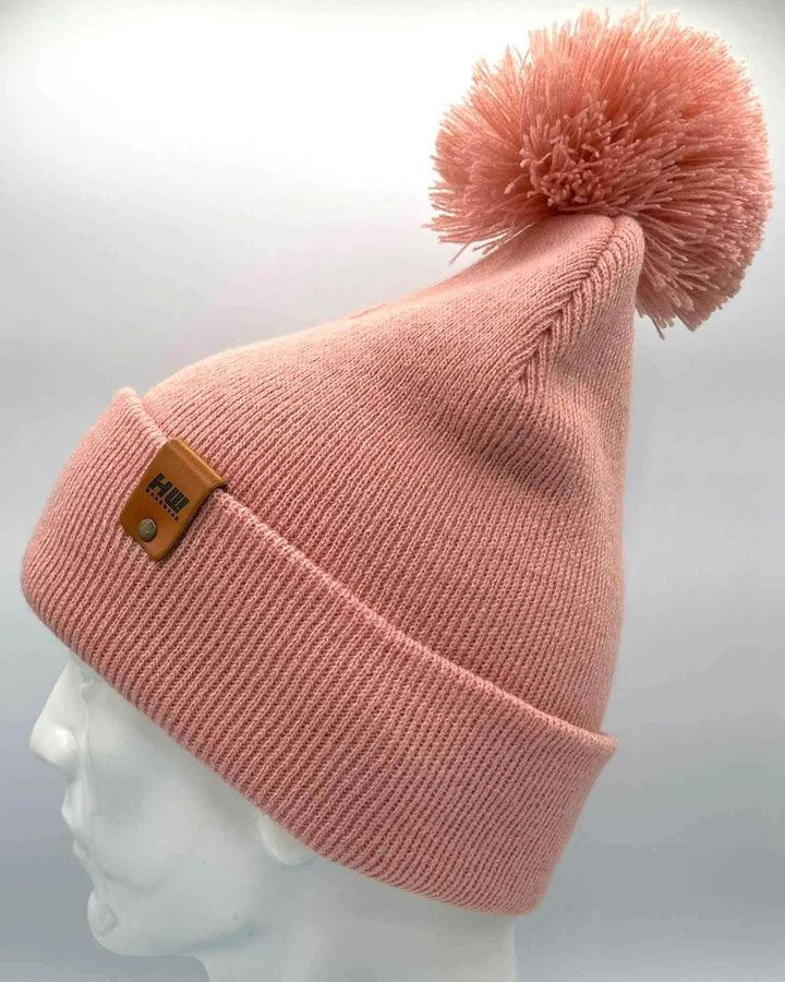 Keep warm and stylish with the HAAKWEAR PomPom Beanie in Pearl Pink, proudly made in the USA. This cozy beanie is perfect for adding a touch of fashion to your winter wardrobe. . Made from 100% Acrylic.