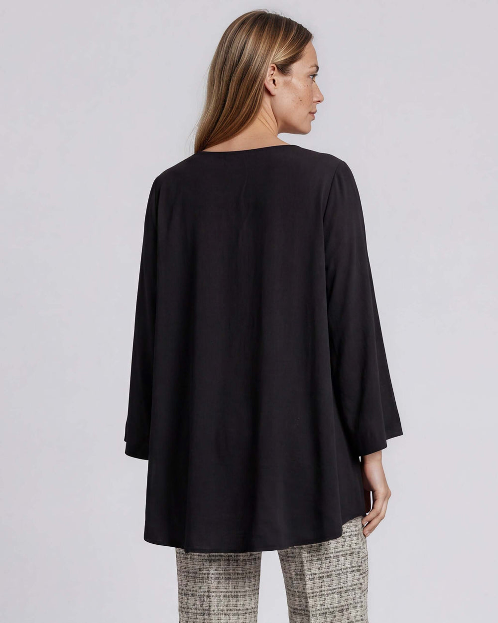 Black dressy V-neck tunic top with mid-length bell sleeves and an overlapping high-low hem that creates a flowy, layered silhouette in lightweight 100% polyester. Made in USA.