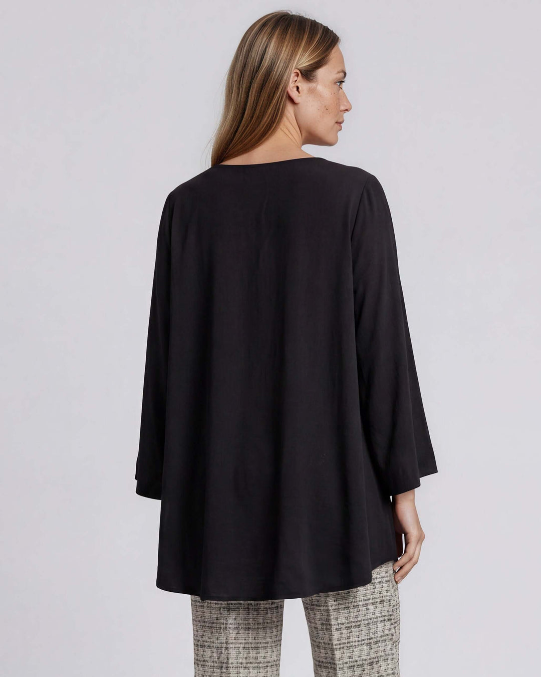 Black dressy V-neck tunic top with mid-length bell sleeves and an overlapping high-low hem that creates a flowy, layered silhouette in lightweight 100% polyester. Made in USA.