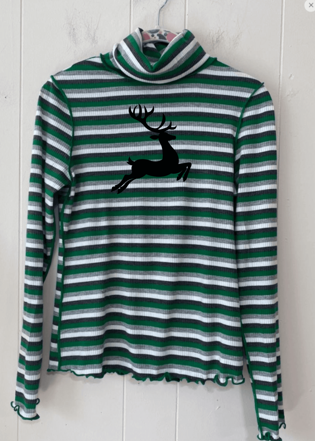Bring holiday cheer to your wardrobe with this whimsical reindeer turtleneck! Featuring a delightful graphic paired with bold stripes in festive red or green, this lightweight ribbed knit top keeps things fun and cozy. The mock turtleneck and semi-fitted cut offer a flattering everyday look, while playful lettuce merrow stitching at the cuffs and hem adds personality
