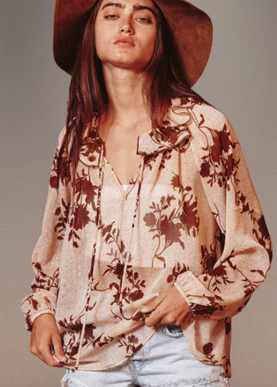 The Presley Lurex Chiffon Floral Ruffle Collar Blouse showcases a sophisticated sheer design in a tan and brown floral print. Its standout smocked high collar and split neckline create an elegant focal point, while long puff sleeves with elasticized cuffs provide refined structure and comfort.  Bucket List Style T1841