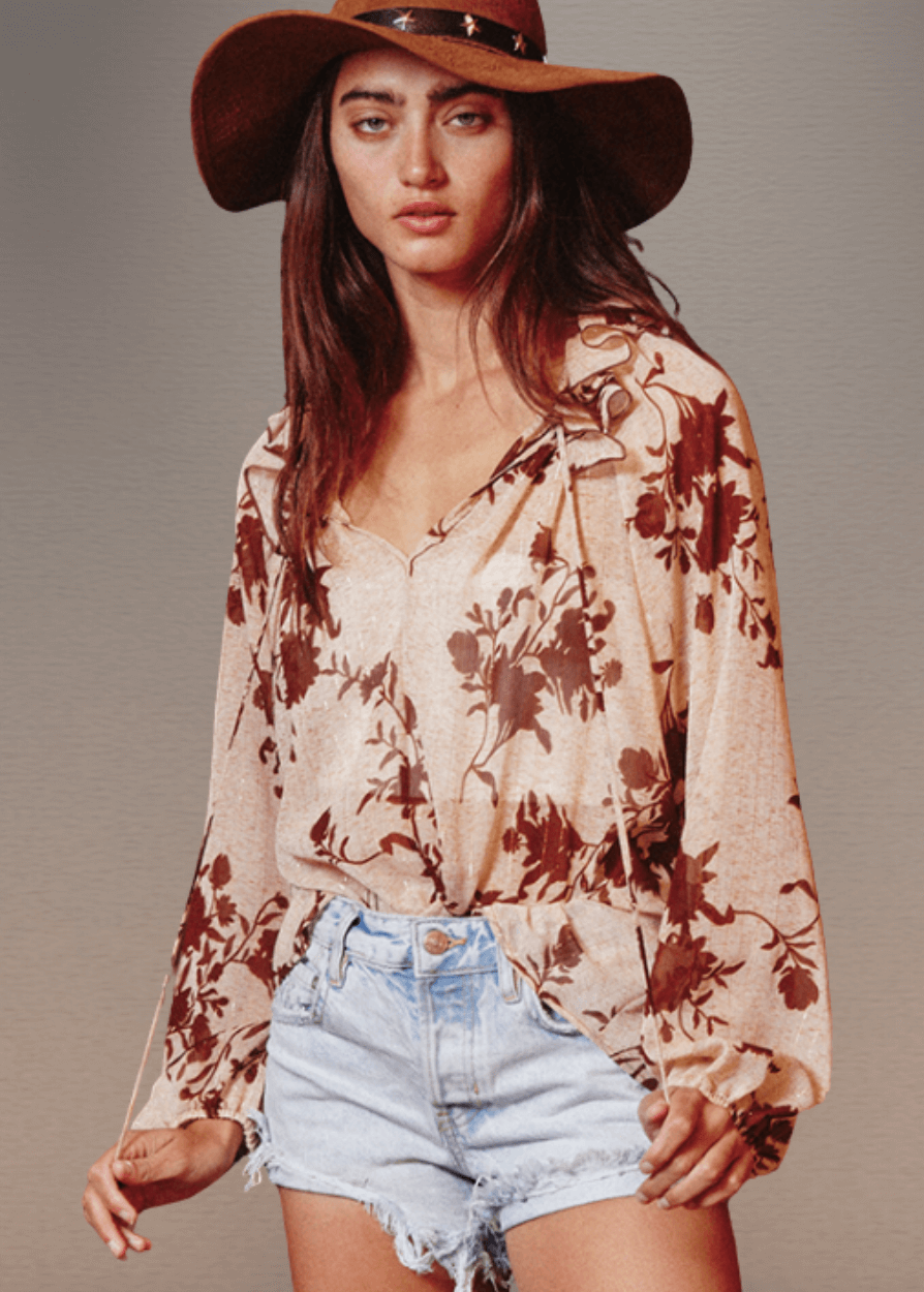 The Presley Lurex Chiffon Floral Ruffle Collar Blouse showcases a sophisticated sheer design in a tan and brown floral print. Its standout smocked high collar and split neckline create an elegant focal point, while long puff sleeves with elasticized cuffs provide refined structure and comfort.  Bucket List Style T1841