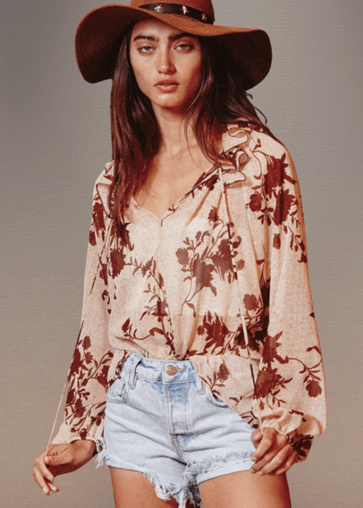 The Presley Lurex Chiffon Floral Ruffle Collar Blouse showcases a sophisticated sheer design in a tan and brown floral print. Its standout smocked high collar and split neckline create an elegant focal point, while long puff sleeves with elasticized cuffs provide refined structure and comfort.  Bucket List Style T1841