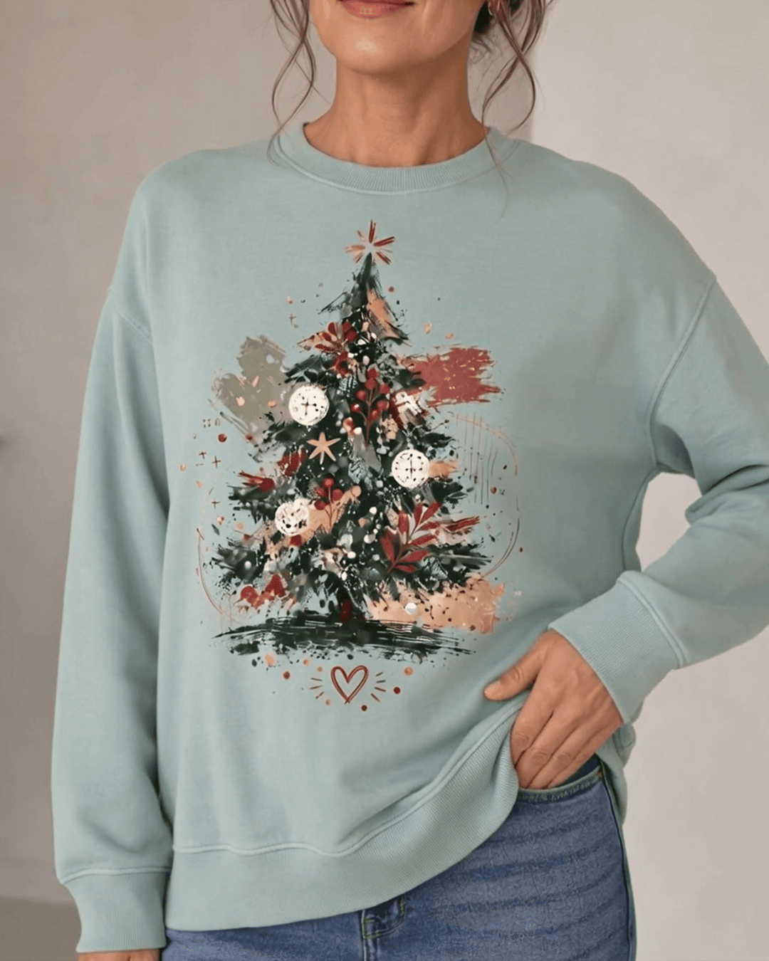 Made in USA Abstract Art Christmas Tree crew neck sweatshirt in sage green with a painterly abstract art Christmas tree graphic, close-up front view of the tree graphic on female model with jeans