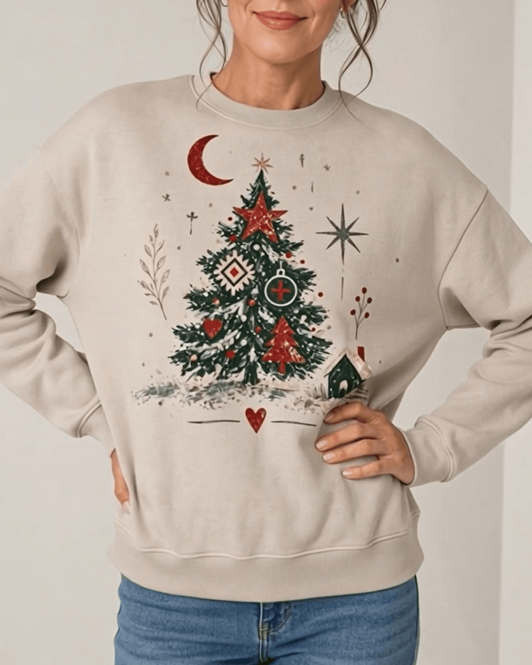 Made in USA Country Christmas Artsy Graphic crew neck sweatshirt in light beige with an artsy folk-art Christmas tree graphic in red, green and cream, close-up front view of the tree graphic on female model with jeans