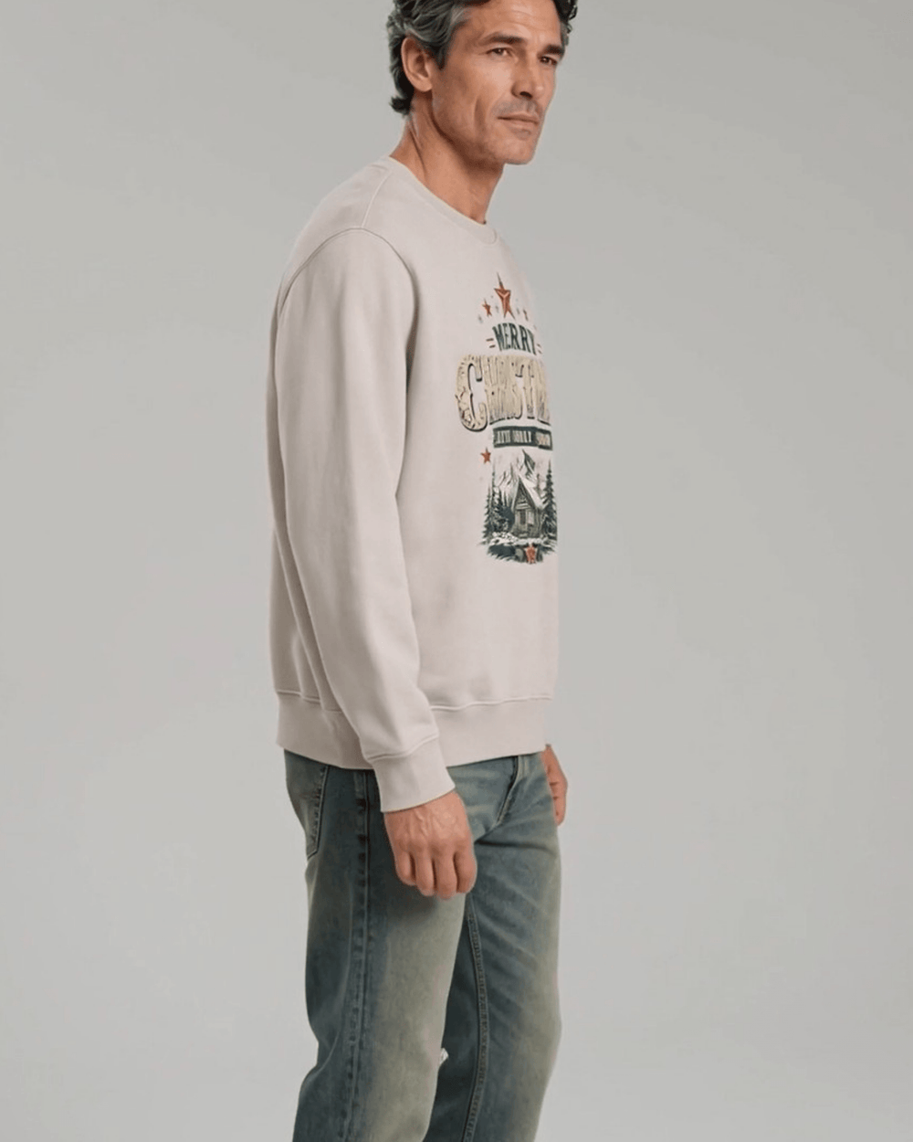 Made in USA Faith Family Freedom Christmas Cabin crew neck sweatshirt in beige with a Merry Christmas Faith Family Freedom log cabin graphic, side view on male model with jeans
