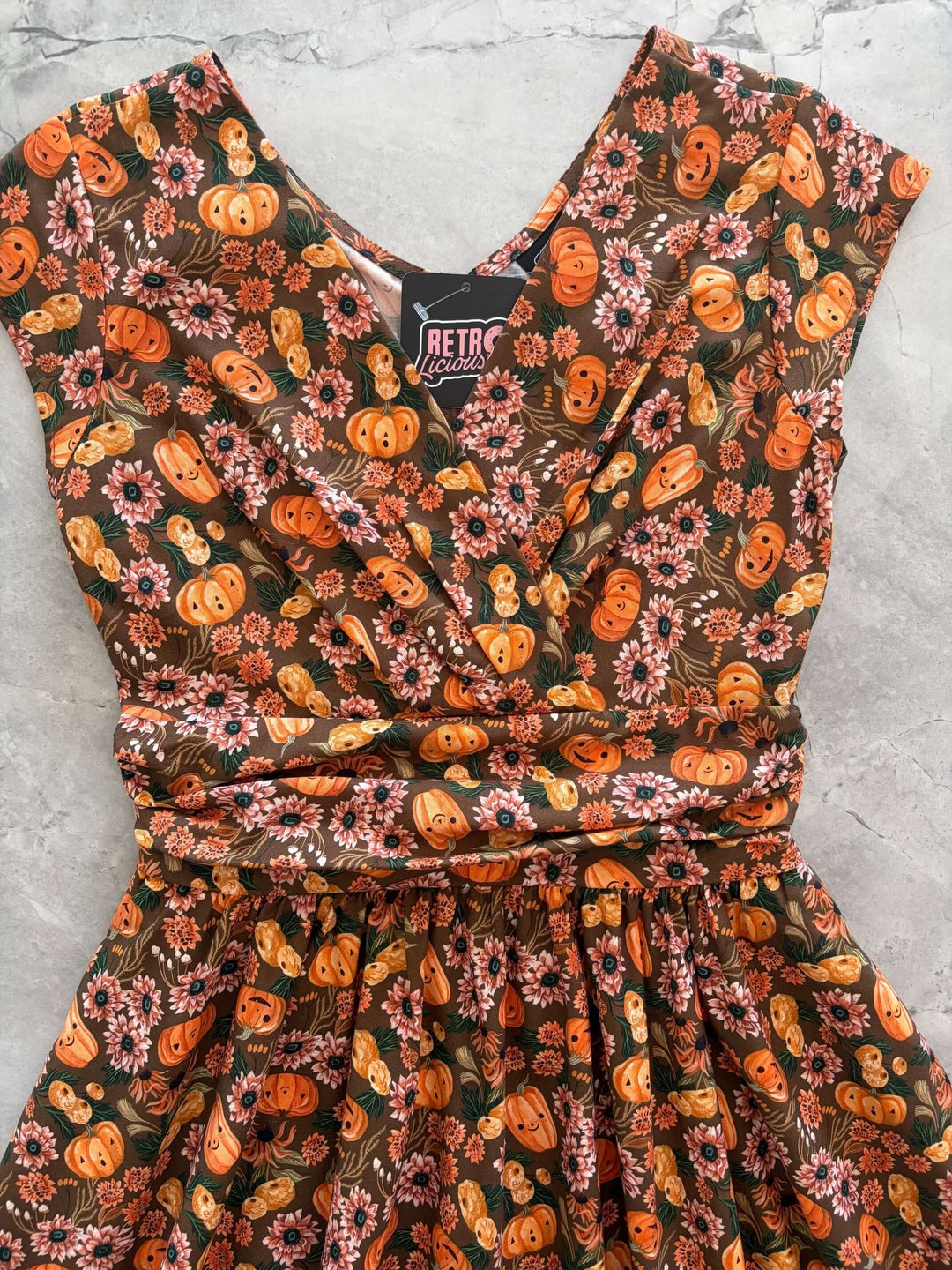 Made in USA by Retrolicious, 100% cotton Greta dress with a V-neck, gathered waist, pockets, and a playful pumpkin-floral print. Sizes XS–4X.