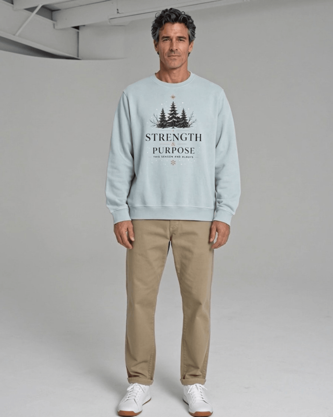 Made in USA Strength and Purpose Holiday Design crew neck sweatshirt in light blue with a Strength and Purpose holiday graphic with navy evergreens and a gold star, front full-length view on male model with khaki pants