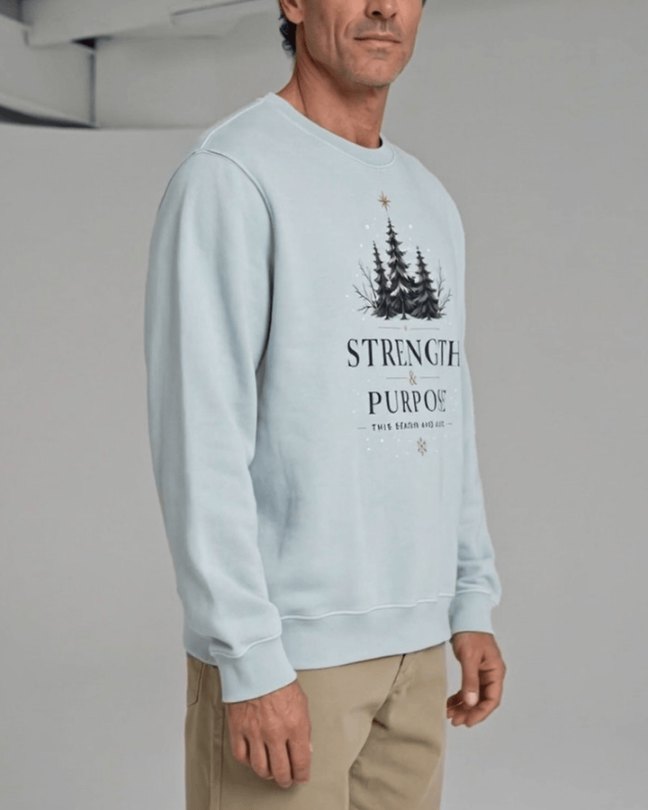 Made in USA Strength and Purpose Holiday Design crew neck sweatshirt in light blue with a Strength and Purpose holiday graphic with navy evergreens and a gold star, three-quarter side view on male model with khaki pants
