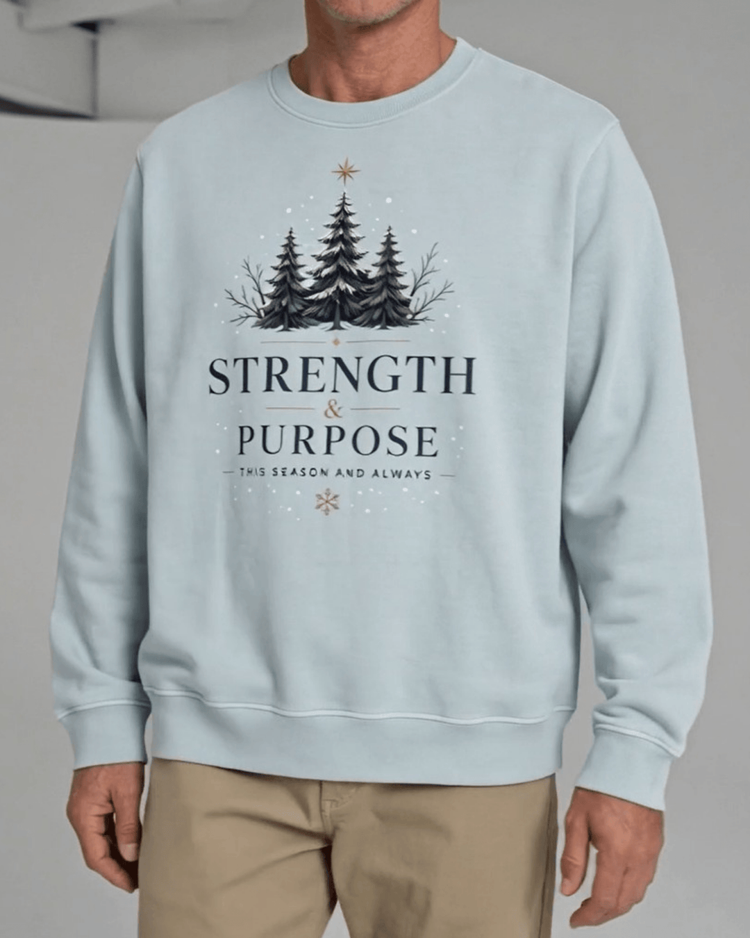 Made in USA Strength and Purpose Holiday Design crew neck sweatshirt in light blue with a Strength and Purpose holiday graphic with navy evergreens and a gold star, close-up front view of the graphic on male model with khaki pants