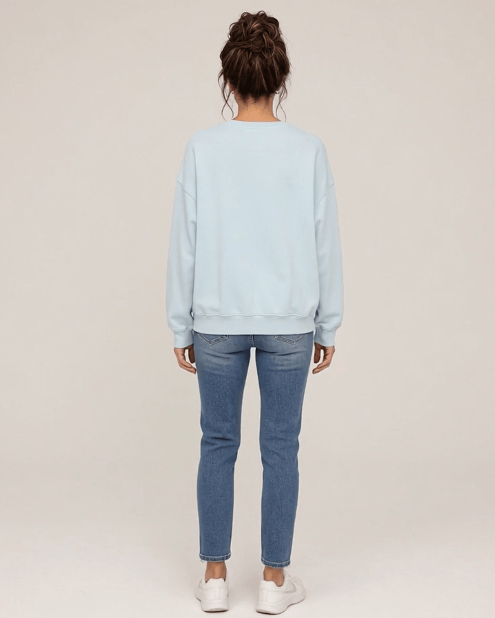Made in USA Vintage Distressed Merry Christmas crew neck sweatshirt in light blue with a distressed charcoal MERRY CHRISTMAS graphic with PEACE JOY LOVE, back full-length view with a plain back on female model with jeans