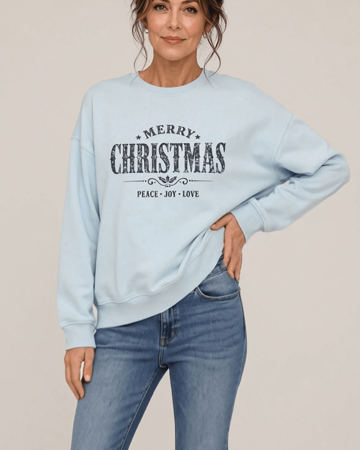 Made in USA Vintage Distressed Merry Christmas crew neck sweatshirt in light blue with a distressed charcoal MERRY CHRISTMAS graphic with PEACE JOY LOVE, front view with hand on hip on female model with jeans