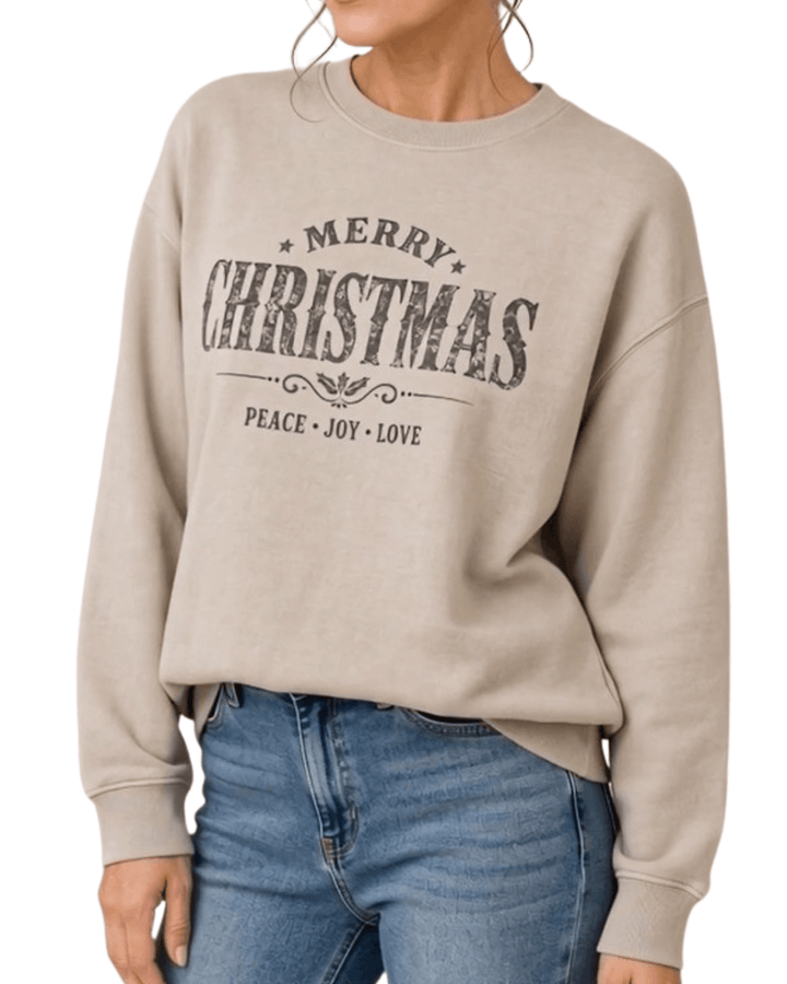 Made in USA Vintage Distressed Merry Christmas crew neck sweatshirt in taupe with a distressed charcoal MERRY CHRISTMAS graphic with PEACE JOY LOVE, front view cropped at the hips on female model with jeans