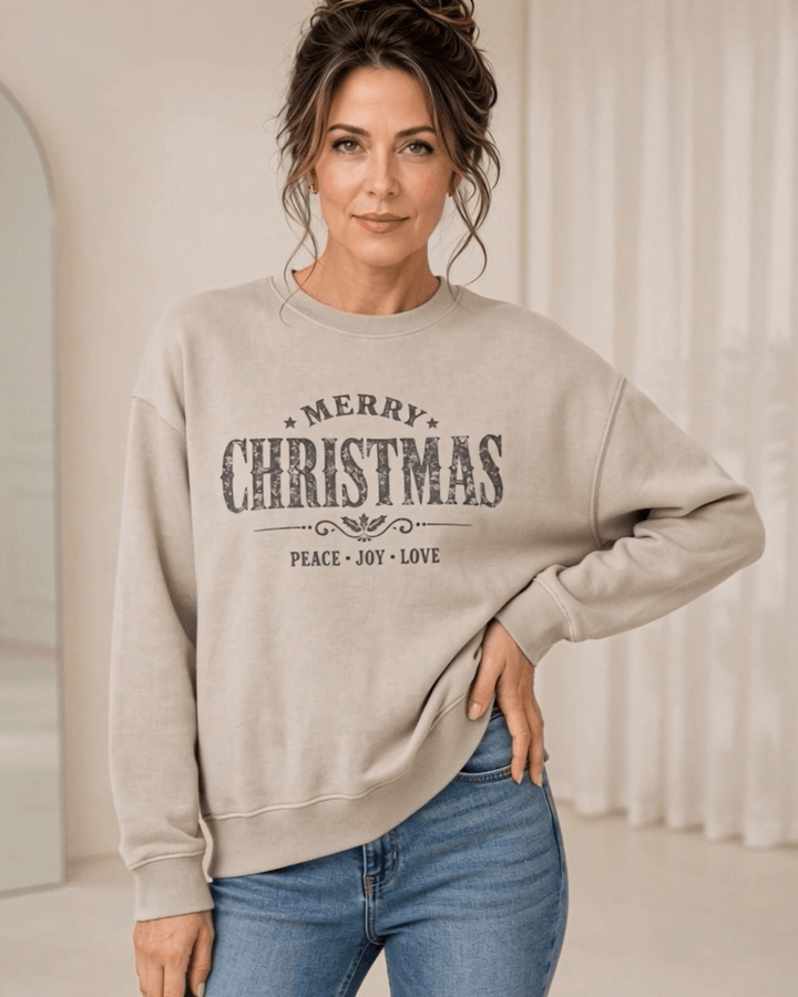 Made in USA Vintage Distressed Merry Christmas crew neck sweatshirt in taupe with a distressed charcoal MERRY CHRISTMAS graphic with PEACE JOY LOVE, front view with hand on hip on female model with jeans