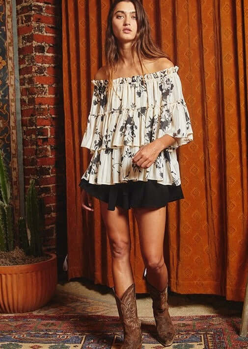 Bucket List Style# T1484 | Ladies Floral Print Tiered Off Shoulder Top with Merrow stitch detailing lurex chiffon in Cream with Black Floral Print | Made in USA